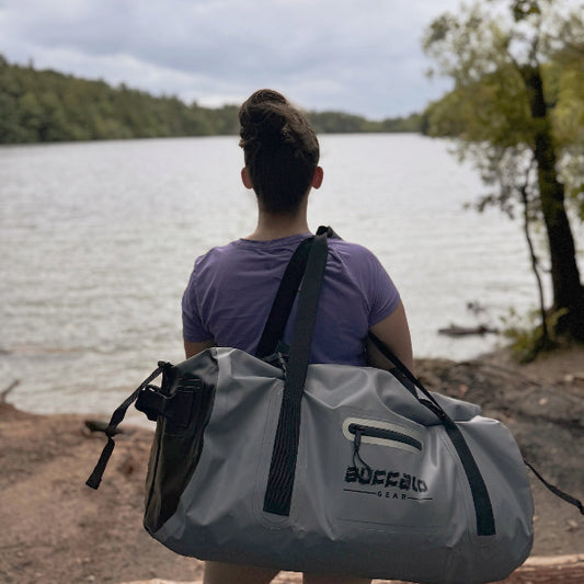 Person with a gray duffel cooler bag by a lake