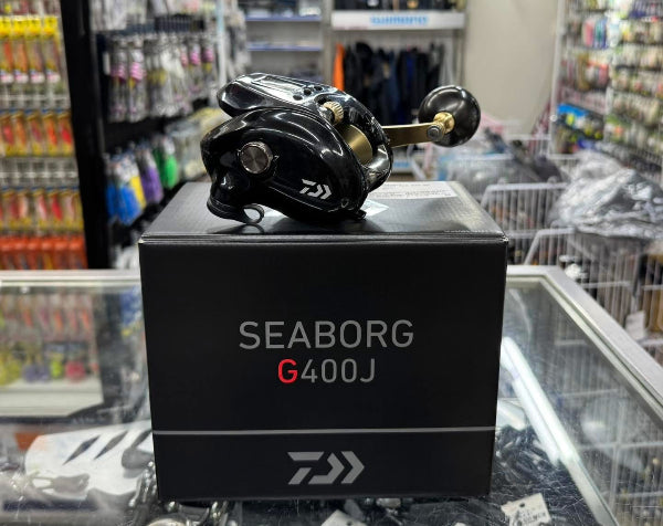 A black Daiwa Seaborg G400J fishing reel resting on top of its black retail box inside a retail store display.