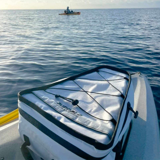 White cooler bag with black lid on a kayak in the water, with another person in a kayak in the background.