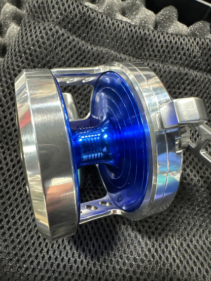 A close-up of a metallic silver and blue spool or reel component resting on a dark gray mesh fabric background.