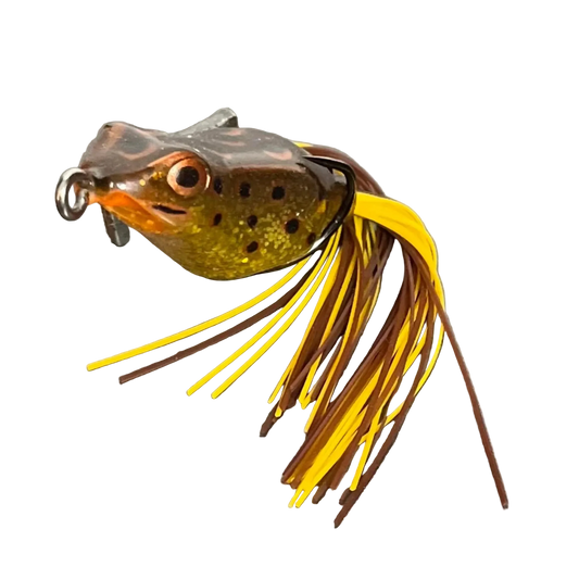 A frog-shaped fishing lure with a realistic head, featuring a yellow and brown skirt with dark brown and yellow strands, photographed on a neutral gray background.