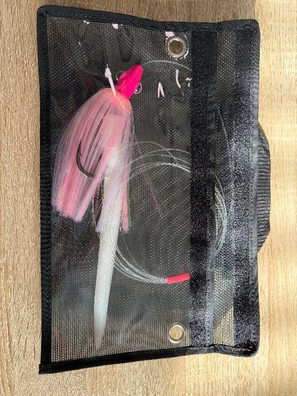 Pink and white fishing lure in a clear pouch on a wooden surface