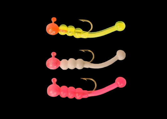 Three soft plastic fishing lures with segmented bodies and hooks, shown vertically on a plain white background. The top lure is translucent yellow-green with an orange head, the middle is pale beige with a pink head, and the bottom is bright pink.